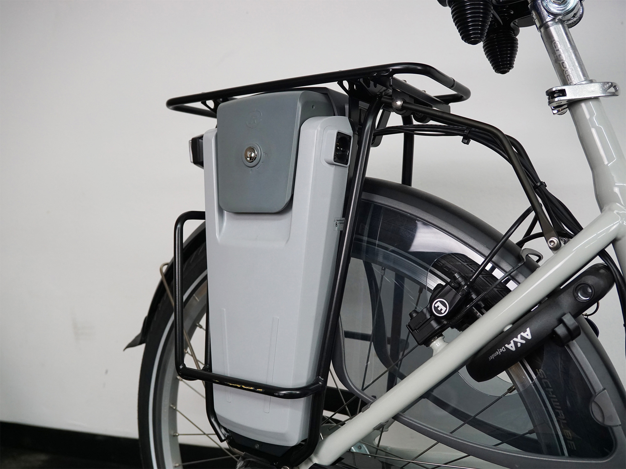 E-Bike mit großem, abschließbarem Akku im Gepäckträger und AXA-Rahmenschloss am Hinterrad.
