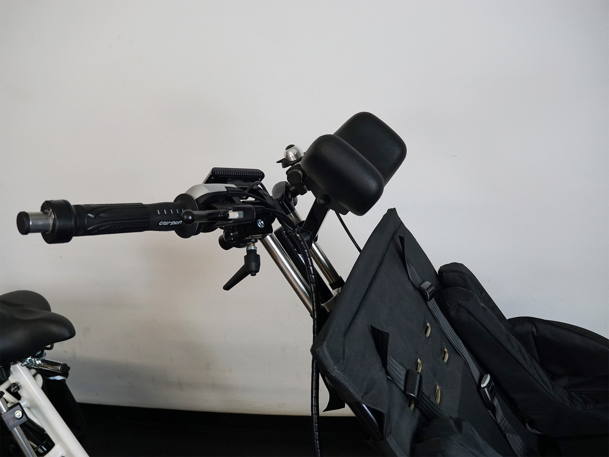 Detailansicht eines Fahrrads mit Kindersitz samt Kopfstütze, daneben Lenker mit Drehgriffschaltung, Klingel und Bremshebel.