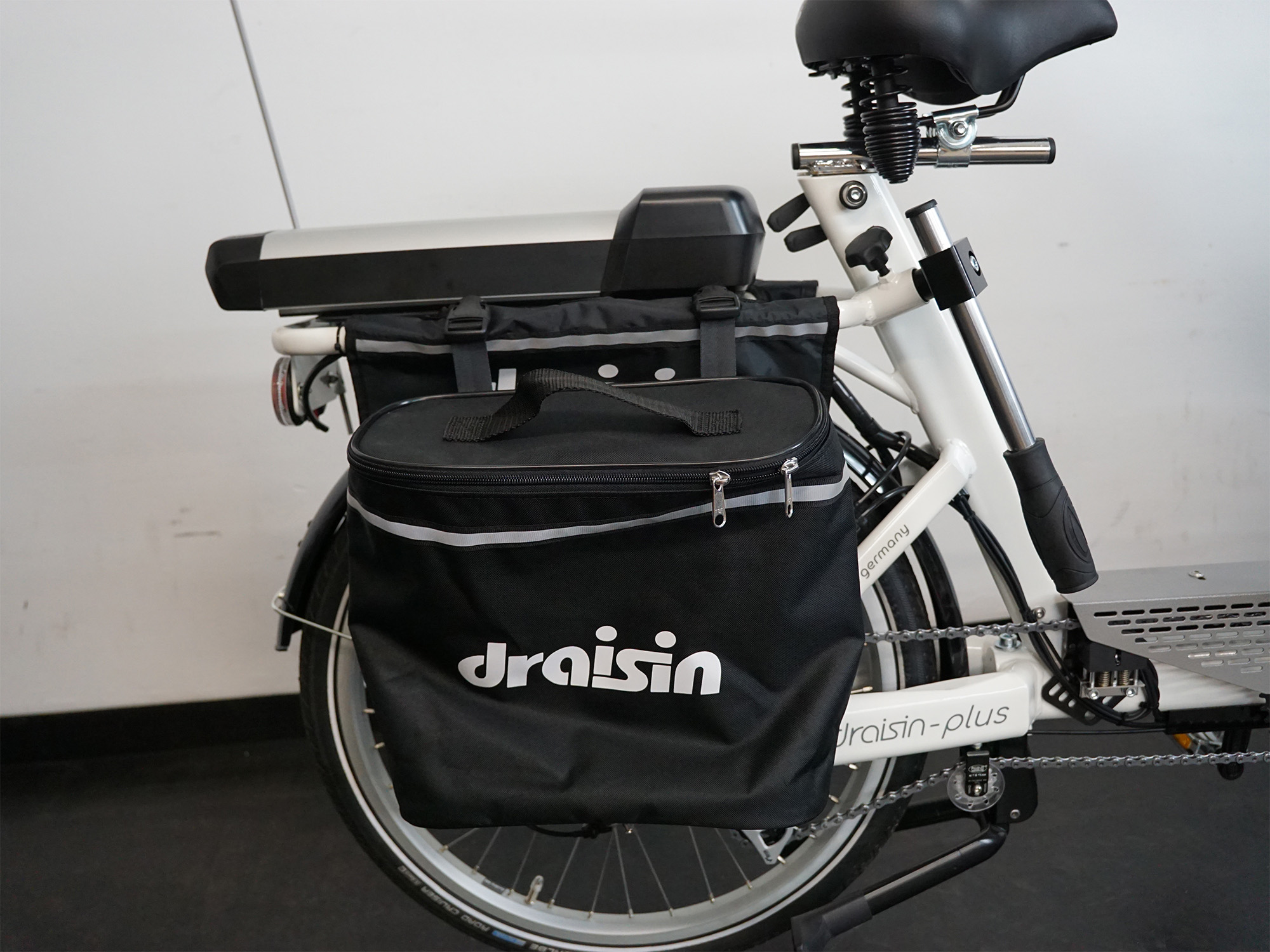 Seitenansicht eines Therapierads mit Tasche „draisin“, Akku am Gepäckträger und stabilem, weißem Rahmen.