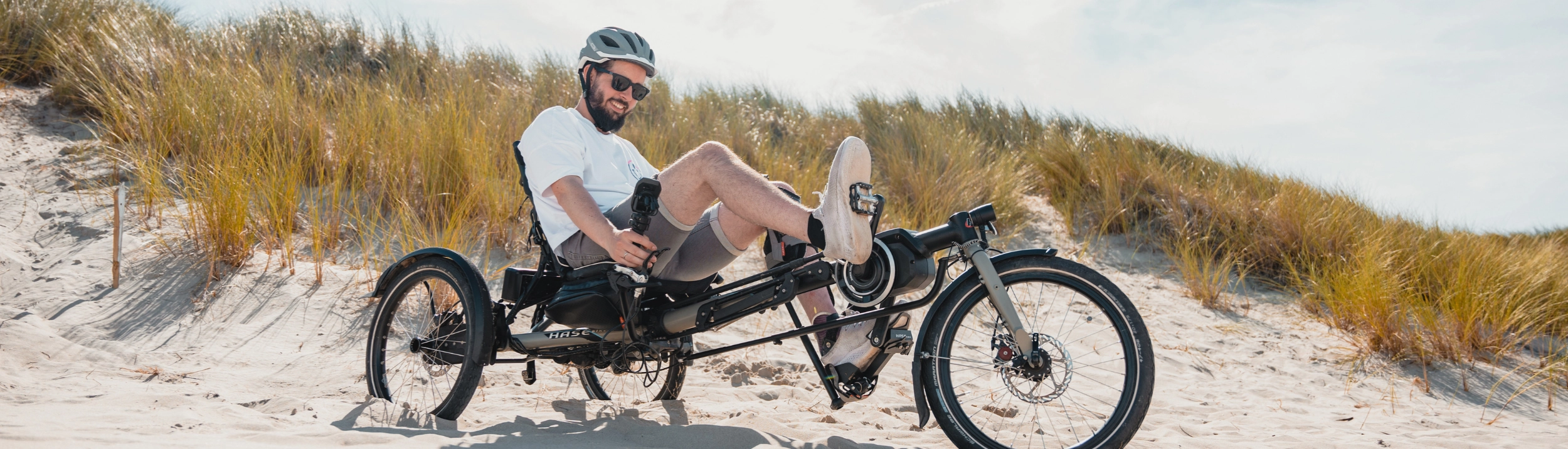 Mann auf einem Liegedreirad zwischen Dühnen
