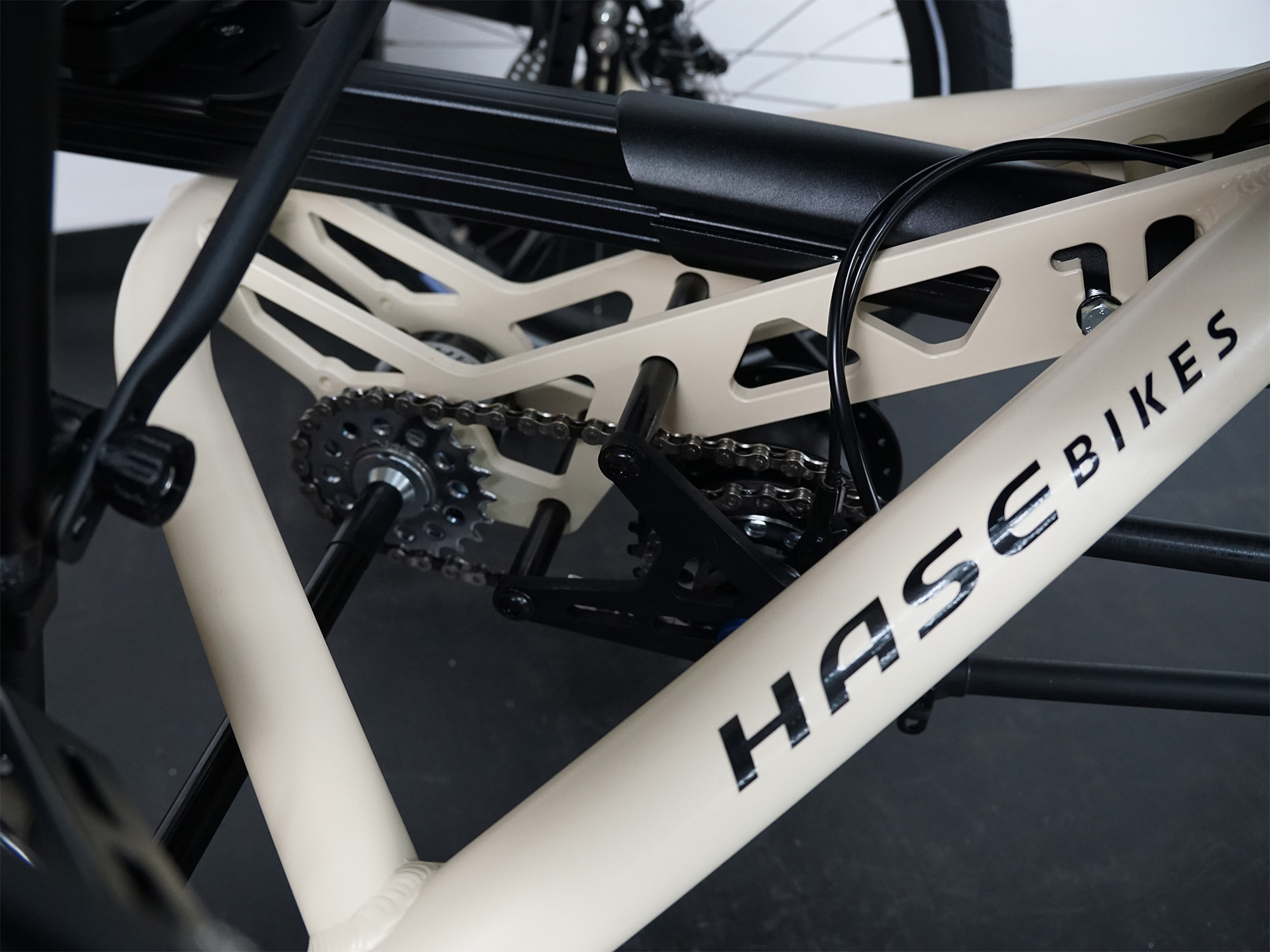Detailansicht eines beigen HASE Bikes Rahmens mit sichtbarem Kettentrieb, Kassette und verstärkter Rahmenstruktur.