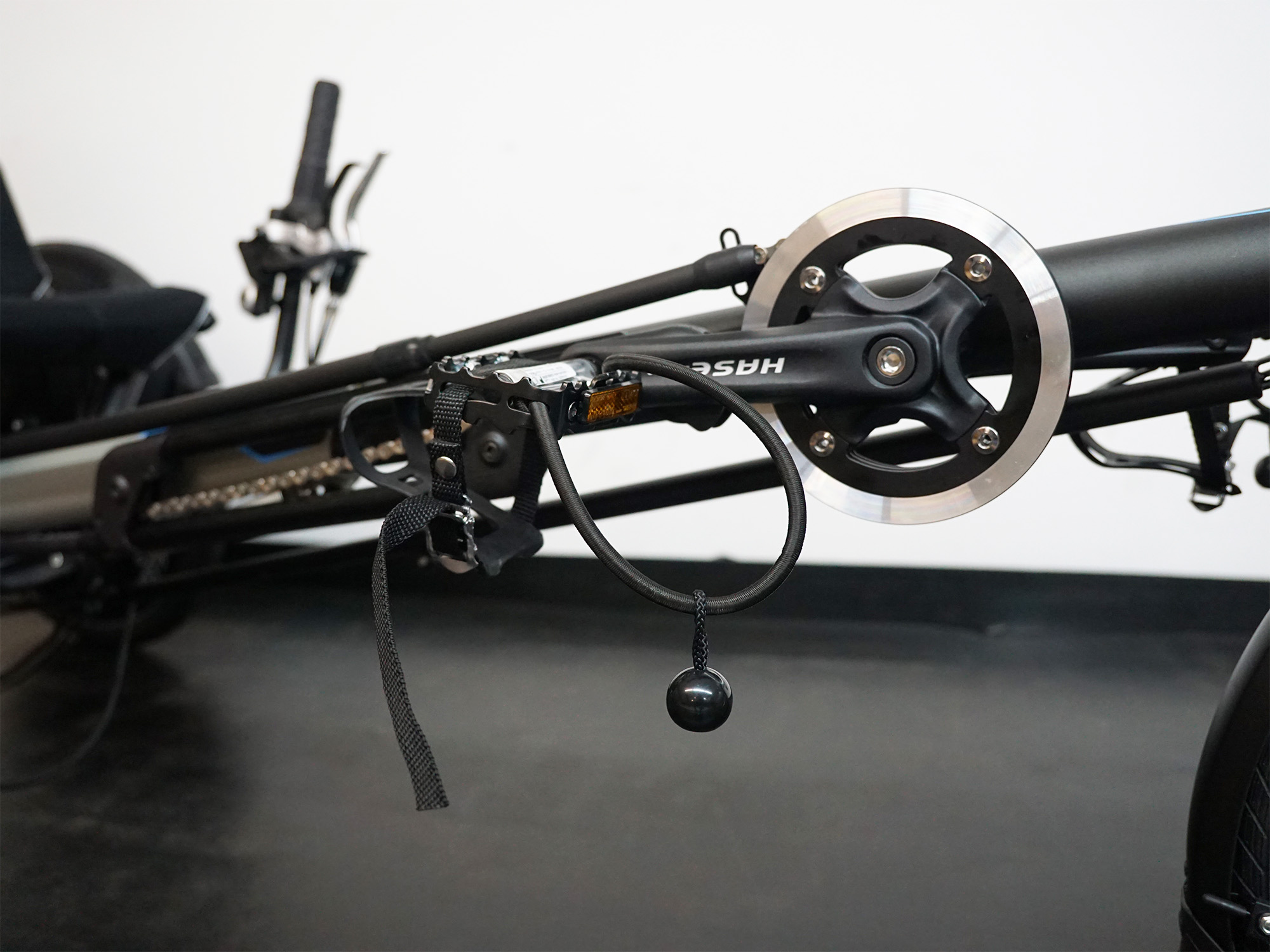 Liegerad mit HASE-Schriftzug, Tretkurbel, Pedal mit Fußfixierung und Schaltmechanik am schwarzen Rahmen.