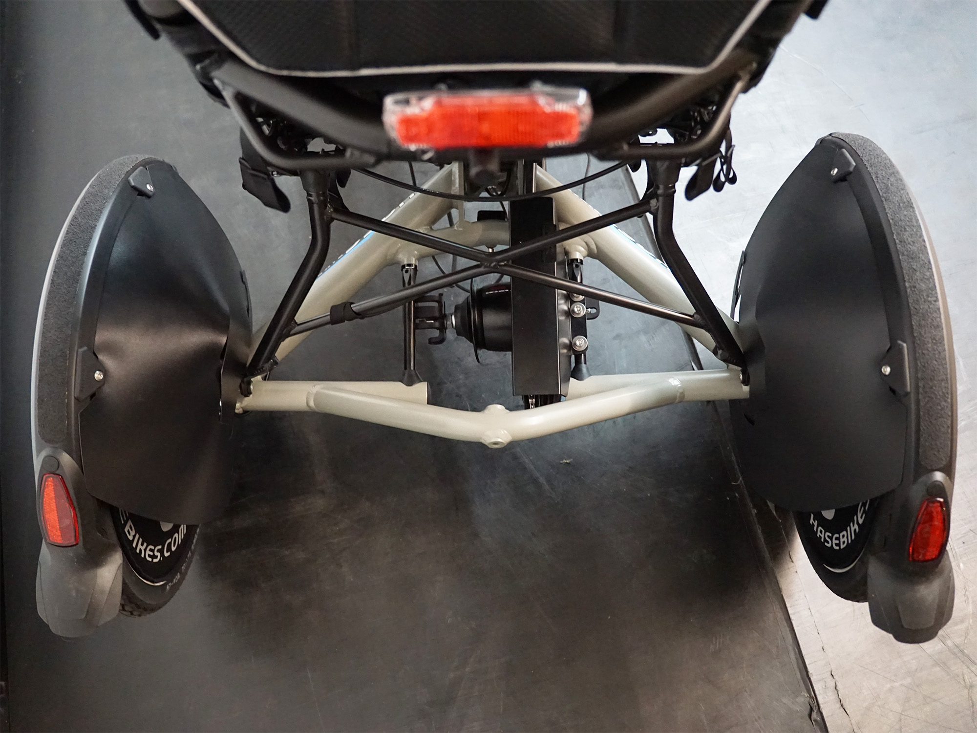 Rückansicht eines Liegedreirads mit Schutzblechen an den Hinterrädern, Rücklicht und stabiler Rahmenkonstruktion.