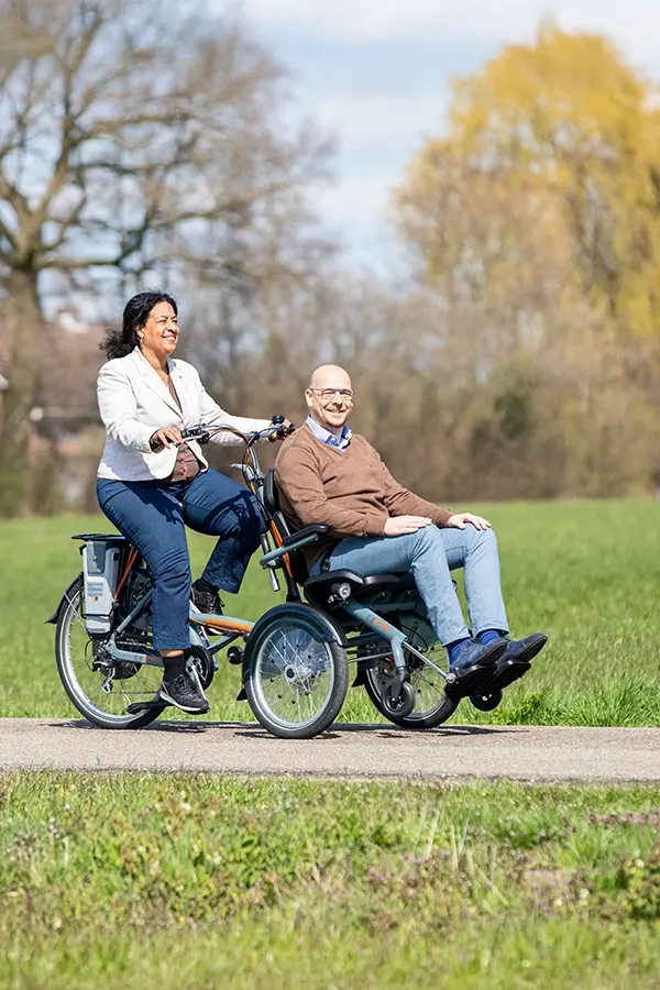 Frau fährt ein Fahrrad wo vorne ein Mann in einem Stuhl sitzt