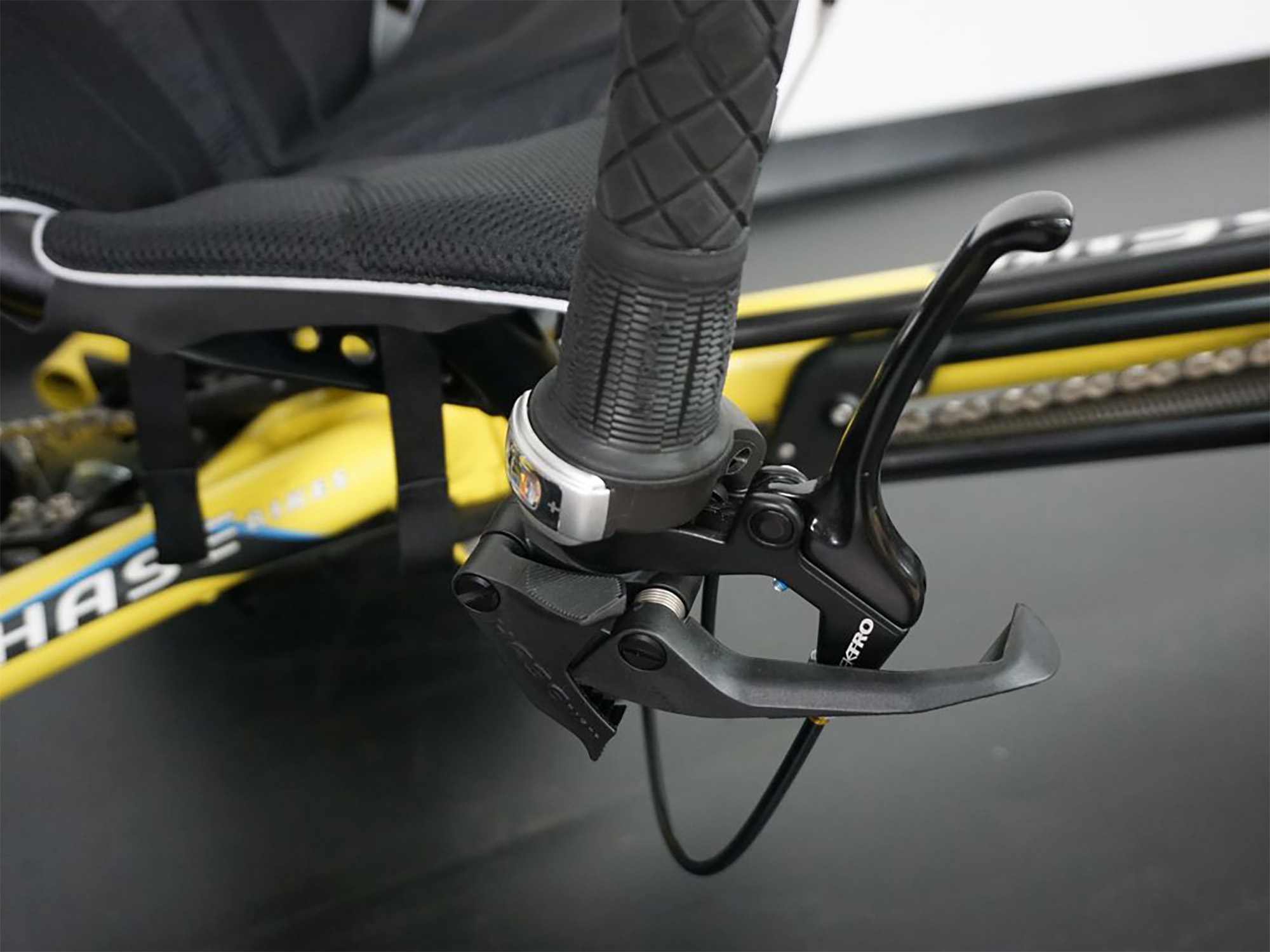 Nahaufnahme eines Liegerads mit gelbem Rahmen, ergonomischem Sitz, Shimano-Bremshebel und Drehgriffschaltung.