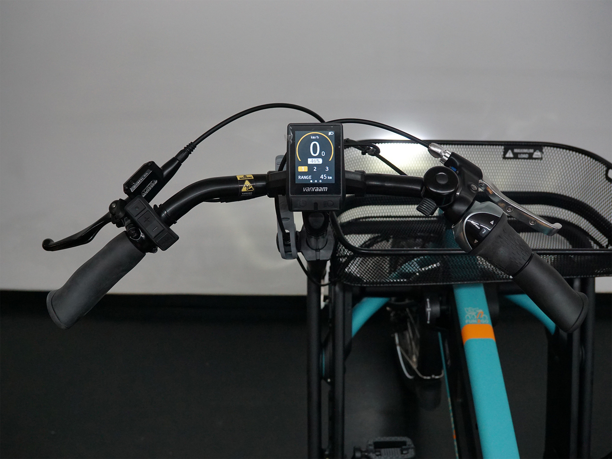 Lenker mit VeoYa-Display, ergonomischen Griffen und Metallkorb an einem türkisfarbenen Dreirad.