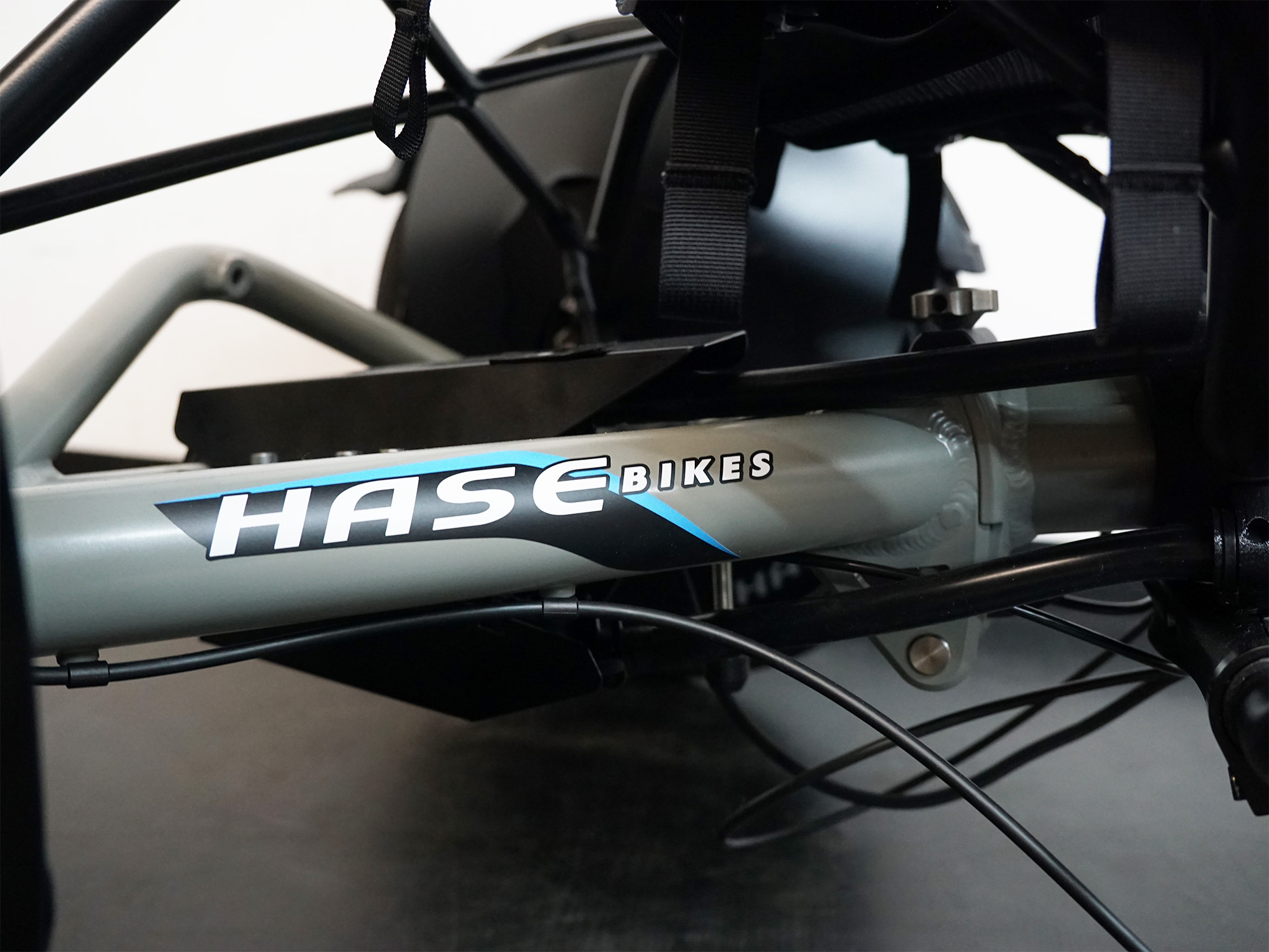 Nahaufnahme des Rahmens eines Liegedreirads mit „HASE BIKES“-Logo, grauer Lackierung und sichtbarer Seilführung