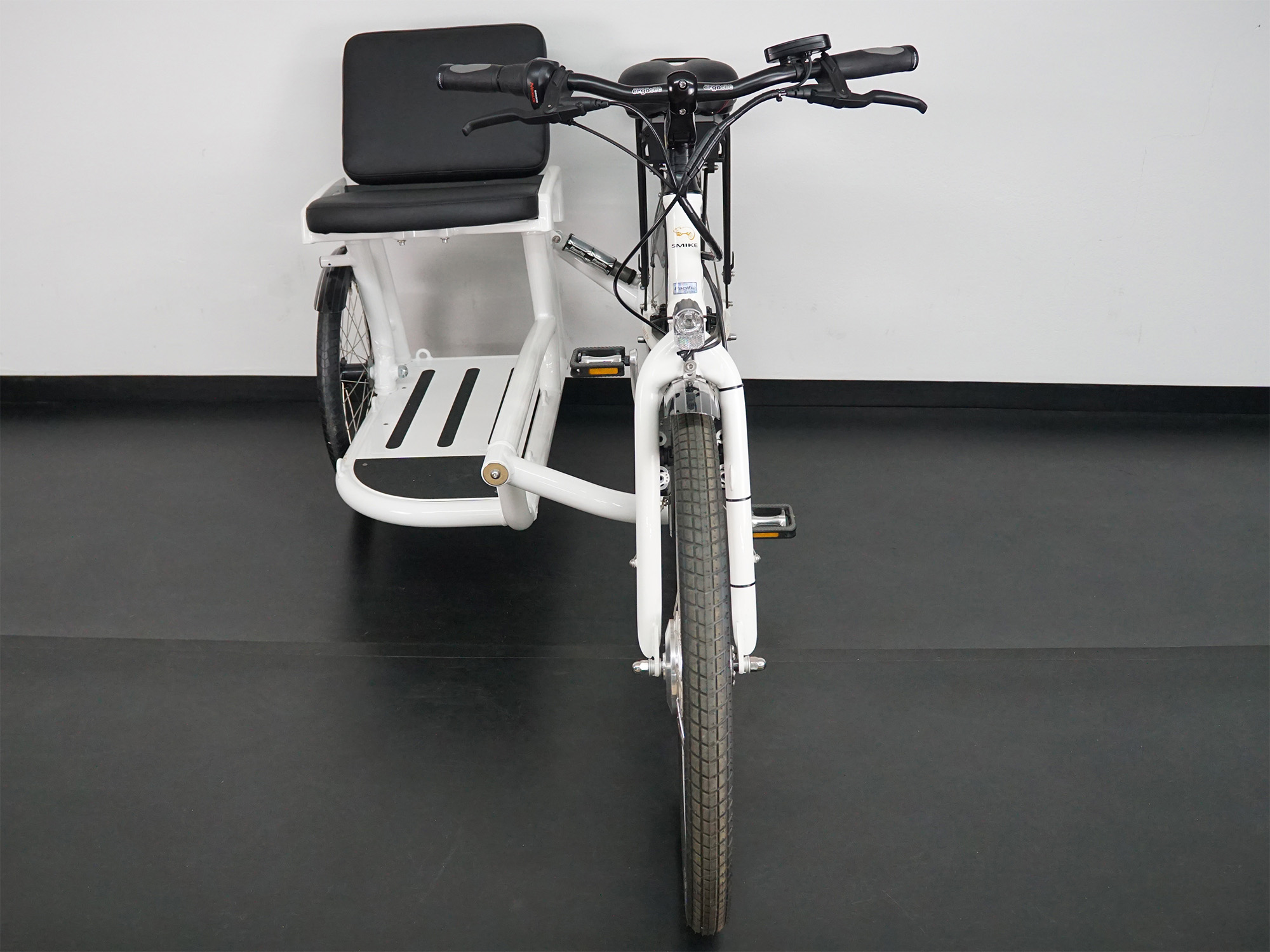 Weißes Dreirad-Lastenfahrrad mit seitlicher Sitzbank für Passagiere und zentralem Lenker.