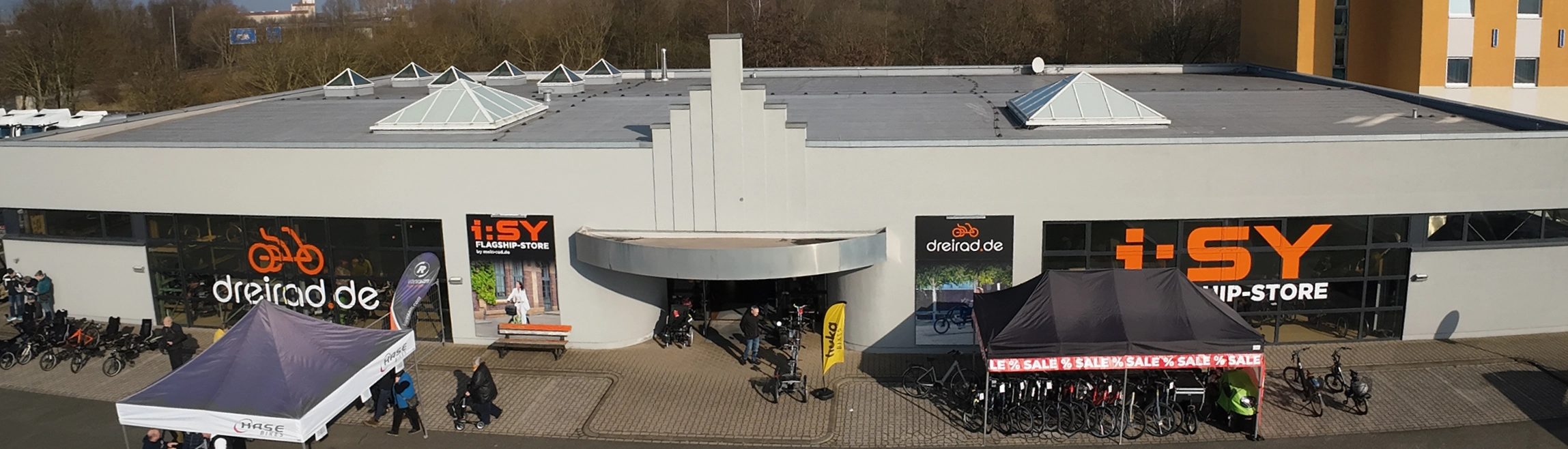 Außenansicht des i:SY Flagship-Stores mit Zelten, Fahrrädern und dreirad.de-Logos.