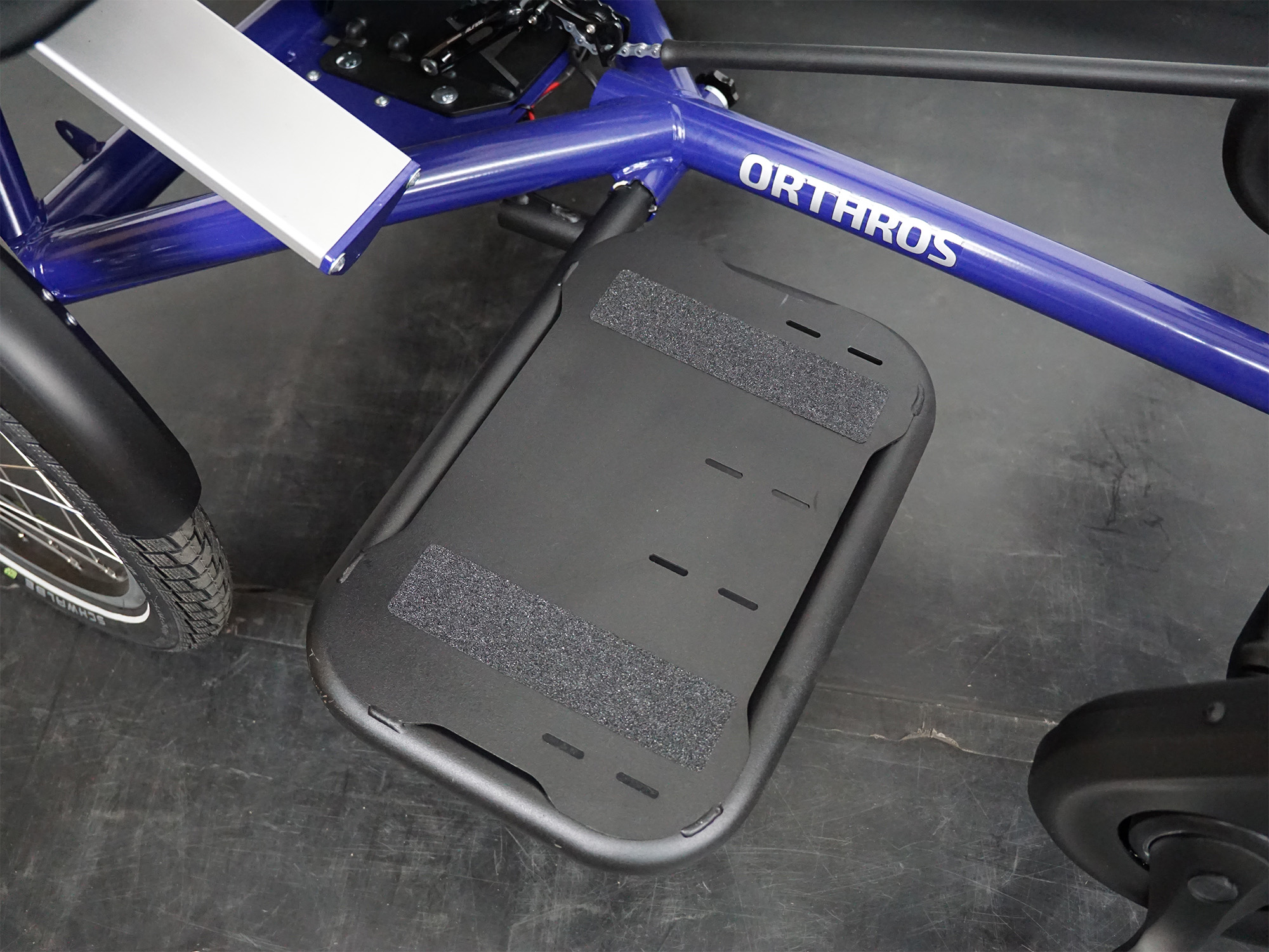 Große Fußablage mit Klettstreifen an einem Spezialrad mit dem Schriftzug „ORTHROS“ am Rahmen.