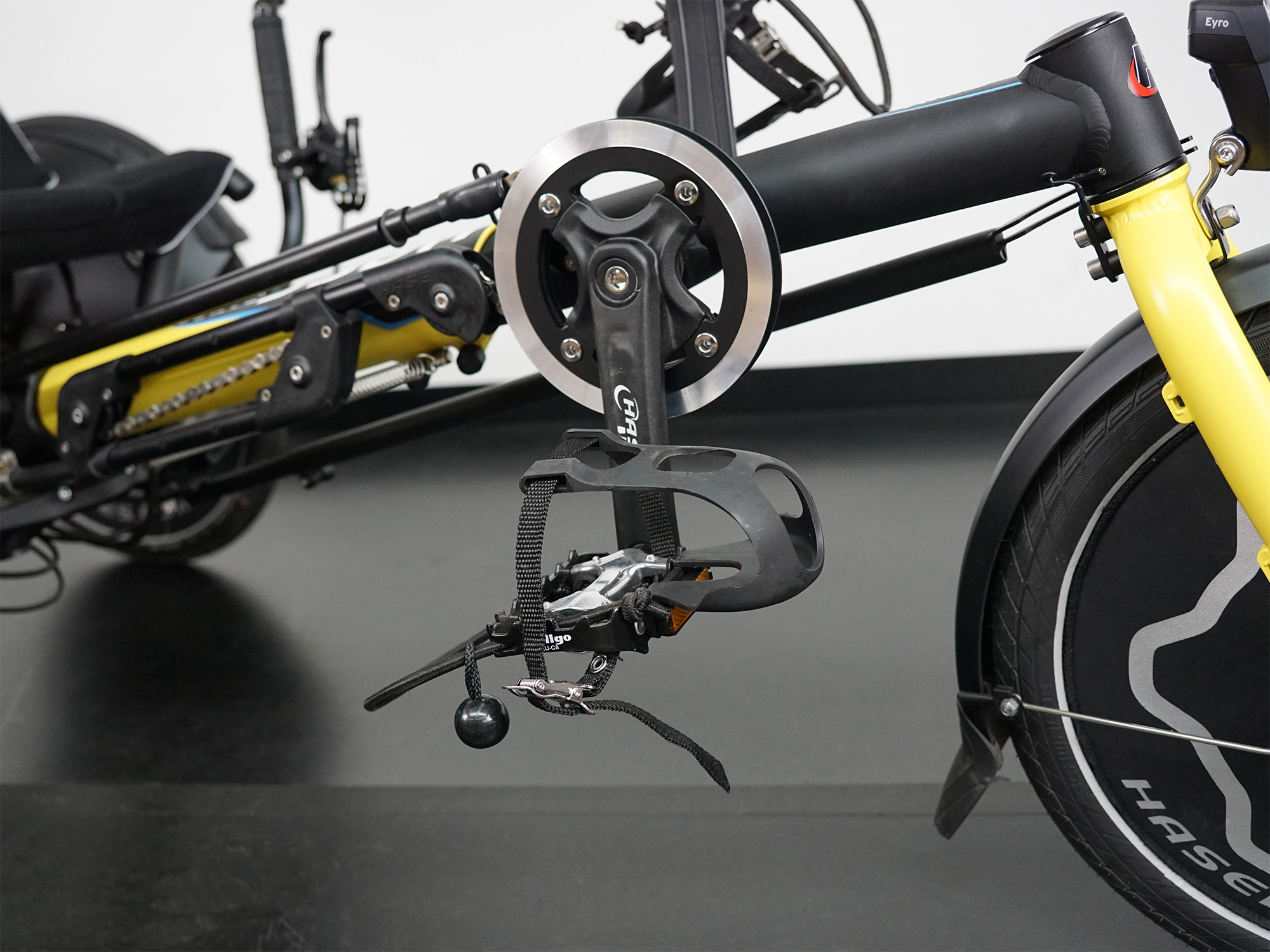 Liegerad mit gelb-schwarzem Rahmen, Kurbelgarnitur, Pedal mit Fußfixierung und HASE-Logo am Vorderrad.