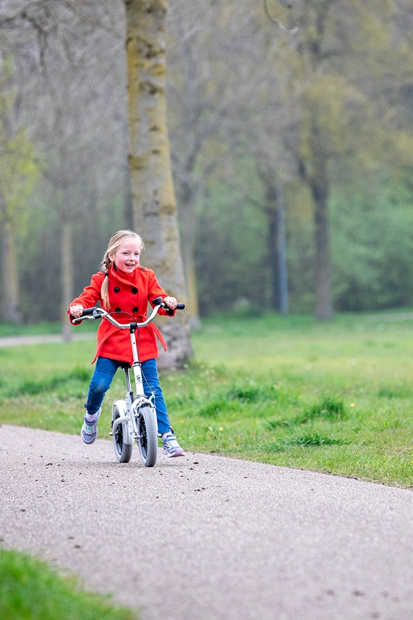 Kind fährt mit einem Laufrad durch die Natur und lacht